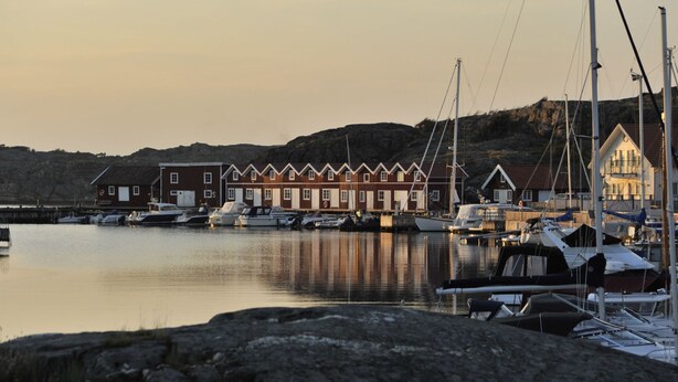 Un port de plaisance avec des bateaux amarrés, une rangée de maisons en bois et une colline en arrière-plan.