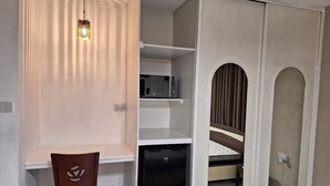 Une pièce de taille modeste, comprenant un bureau, une chaise, une armoire avec un miroir et un petit appareil électroménager noir.