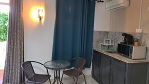 Une petite cuisine équipée d’un four à micro-ondes, d’une machine à café et d’une petite plante en pot. On y trouve deux chaises et une table, et un rideau sépare l’espace.