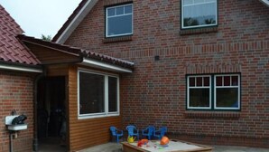 Une maison en briques avec une terrasse en bois, un espace de jeux avec des jouets et une fenêtre.