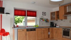 Une cuisine avec des meubles de rangement en bois, une cuisinière et une fenêtre avec des stores rouges.