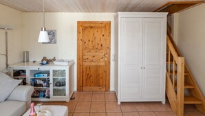 A cozy living room with a wooden ceiling, a white sofa, a bookshelf, a wooden door, and a white wardrobe. - in Dänschendorf auf Fehmarn by Interhome (Bannesdorf)
