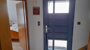 A room with a blue door, a bed with white bedding, a small wall-mounted shelf, and a window. - Moderne Ferienwohnung mit Balkon in Strandnähe by Interhome (Friedrichskoog)