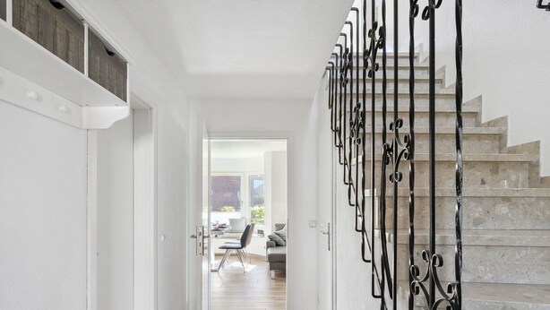 Ein modernes Interieur mit einer Treppe, einem zur Wohnbereich führenden Flur und Blick ins Freie.