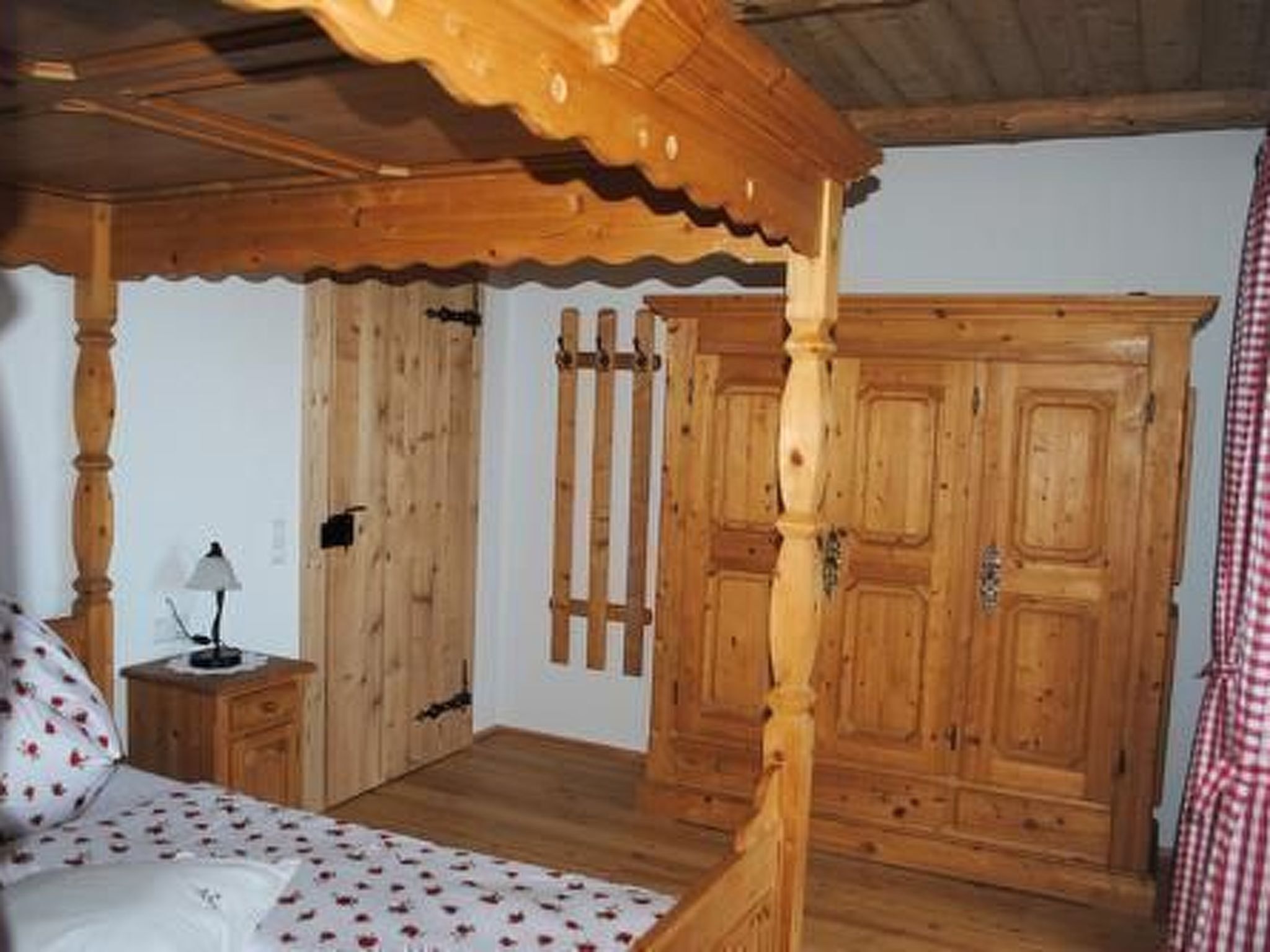 Un lit à baldaquin en bois, recouvert d’une courtepointe blanche, une table de chevet avec une lampe et une armoire en bois dotée d’un miroir.