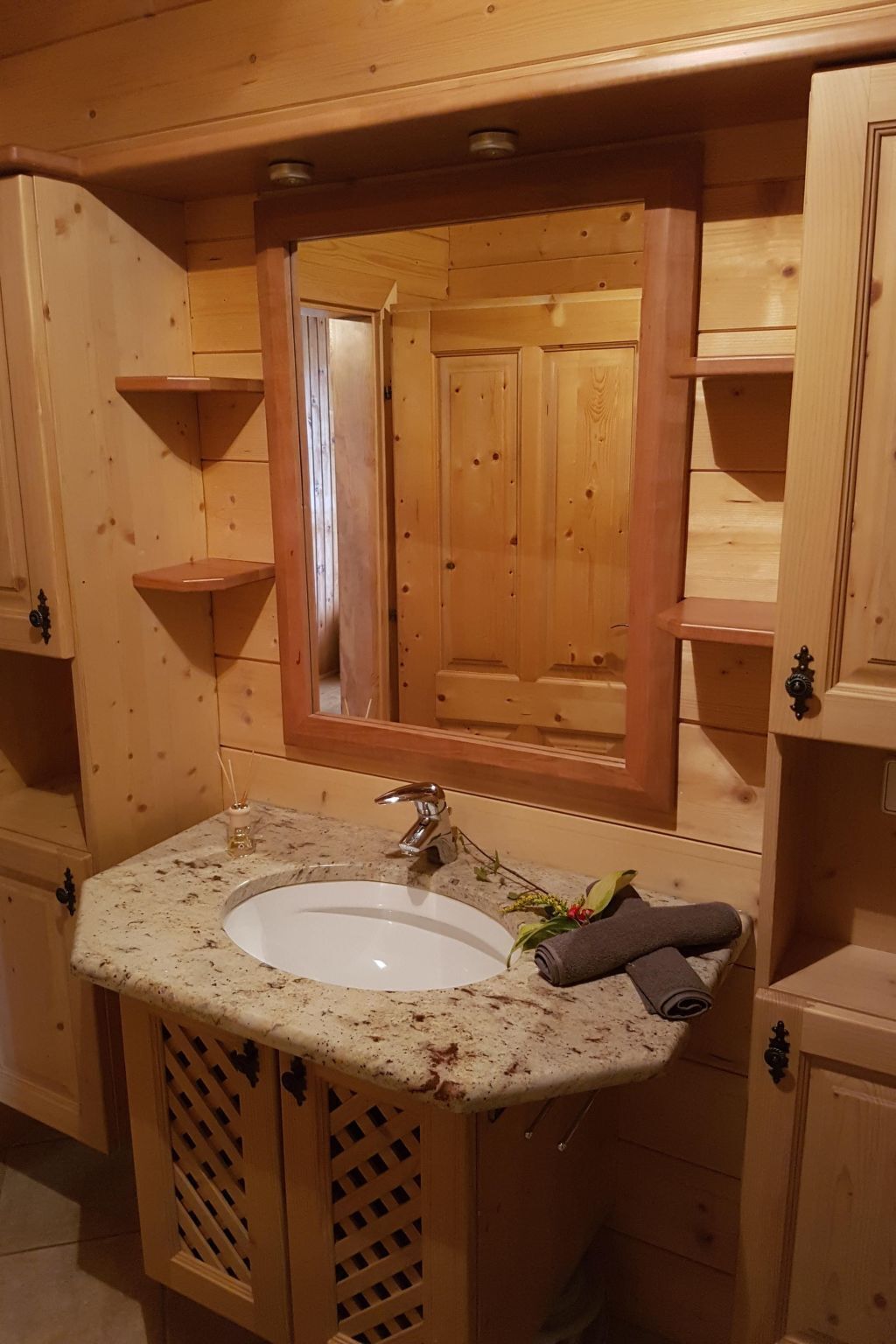 Un baño de madera con lavamanos de granito, un espejo y armarios de madera.