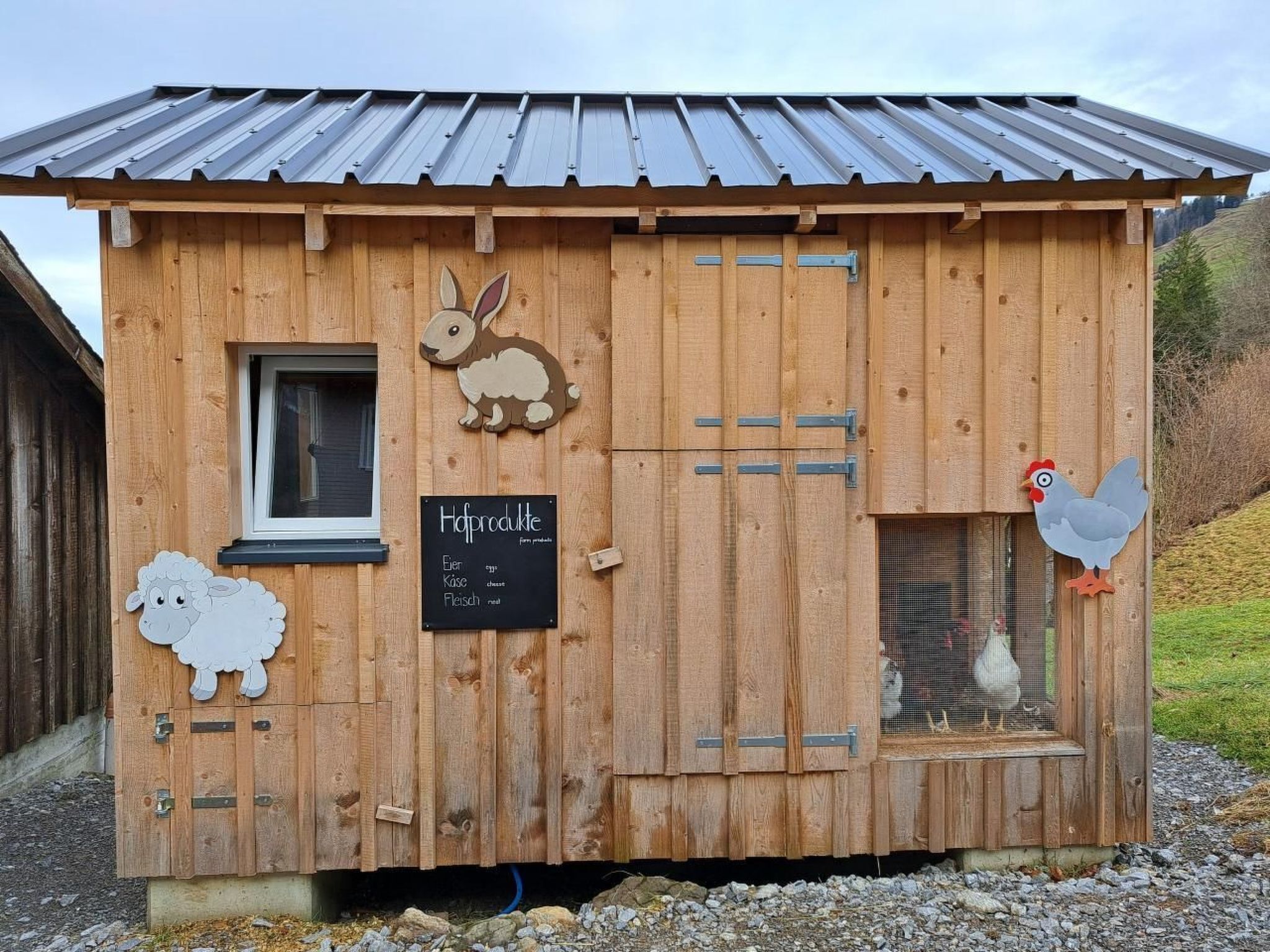 Une construction agricole en bois, dotée d’un toit en métal, d’une fenêtre, d’une porte et d’un panneau noir où sont énumérés les produits de la ferme.