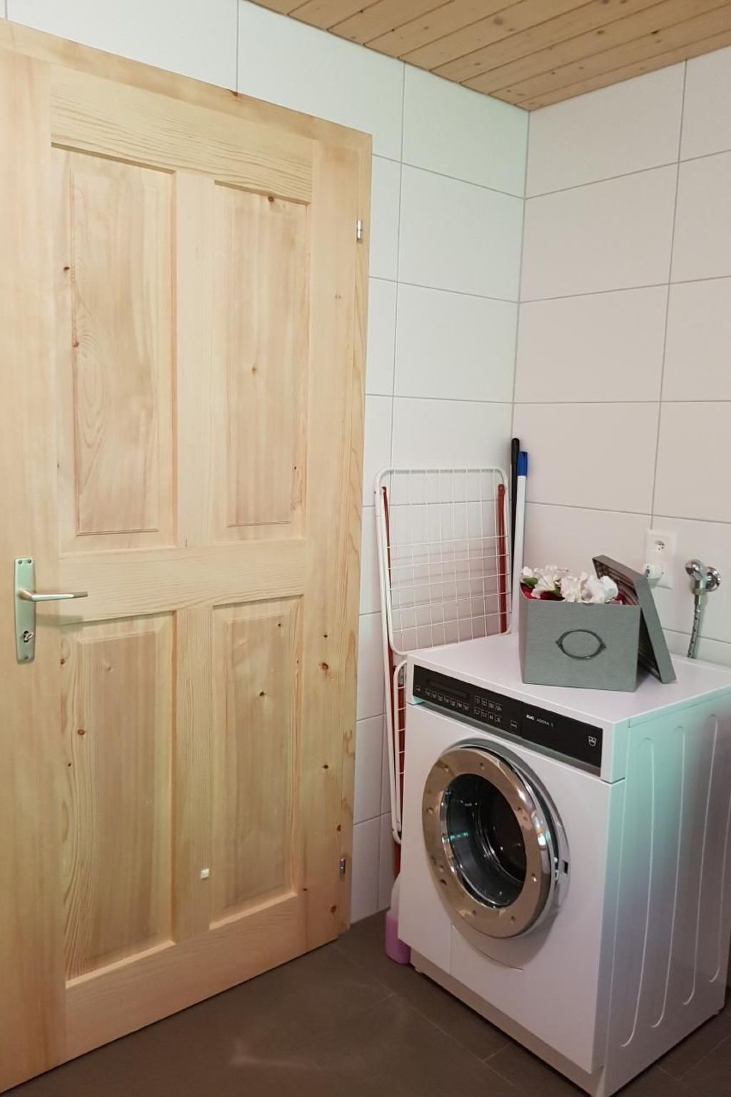 Ett tvättrum med en tvättmaskin, ett torkställ och en dörr av trä.