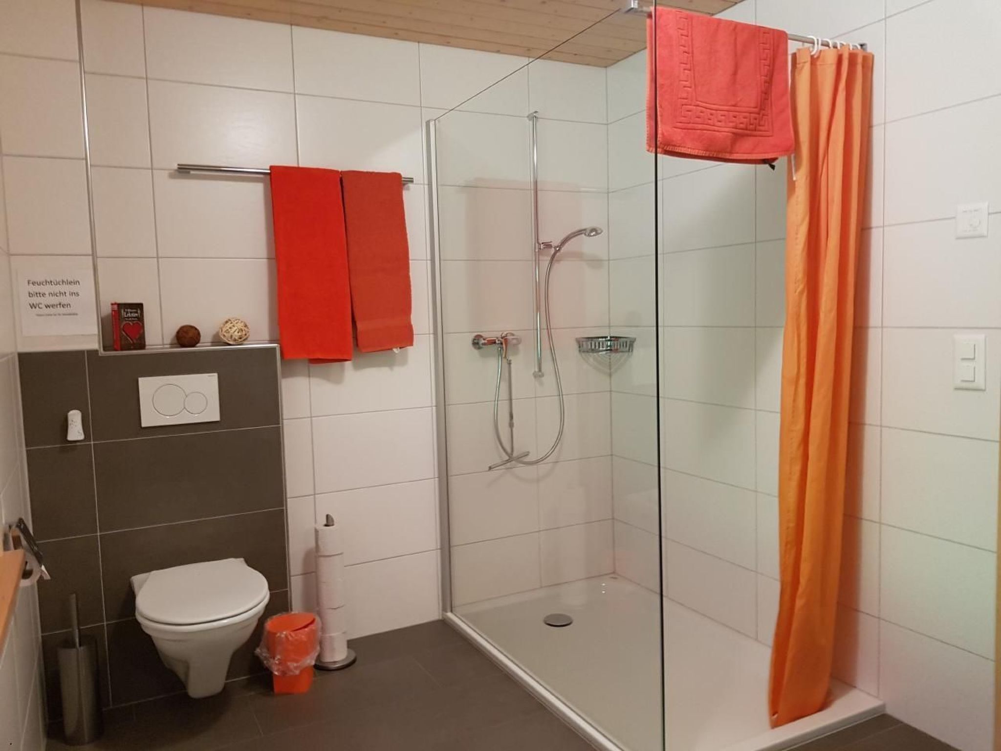A bathroom with a toilet, a shower with a glass door, and two red towels hanging on a rack.