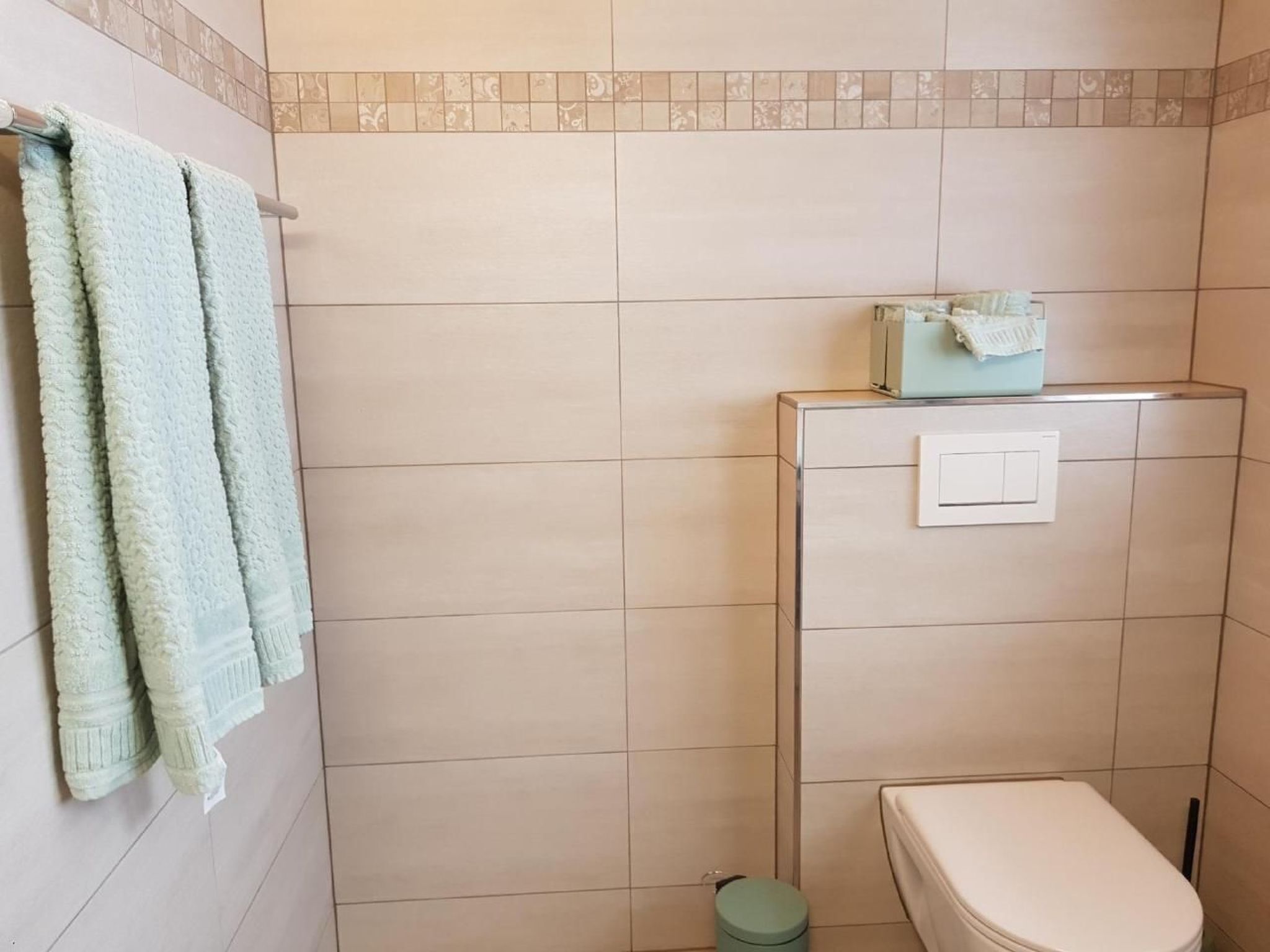 Ein Badezimmer mit Toilette, Handtuchhalter mit Handtüchern, Mülleimer und Lichtschalter an der Wand.