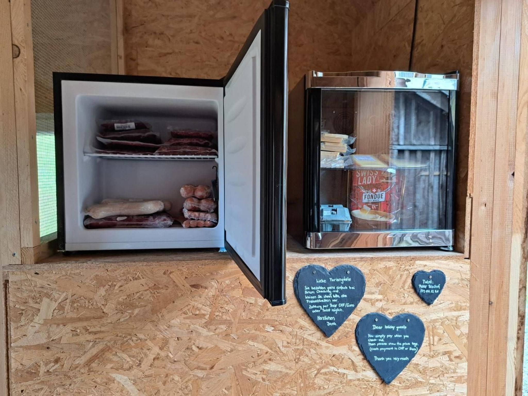 L’intérieur est en bois et comprend un réfrigérateur contenant divers aliments, ainsi qu’une vitrine en verre où sont exposés différents fromages. On y trouve également des panneaux en forme de cœur portant des messages.