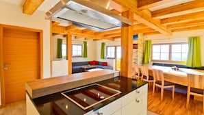A modern kitchen with a central island, wooden beams, and a dining area with a table and chairs. - Das Almhaus in Bad St. Leonhard im Lavanttal by Interhome (Klippitztörl)