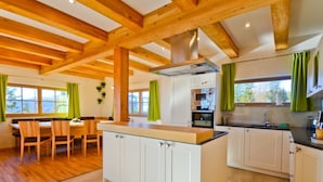 A modern kitchen with wooden beams, white cabinets, and a dining area with a wooden table and chairs. - Das Almhaus in Bad St. Leonhard im Lavanttal by Interhome (Klippitztörl)