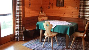 Interior de una cabaña de madera con una mesa de comedor, dos sillas, un banco y una ventana con cortinas.
