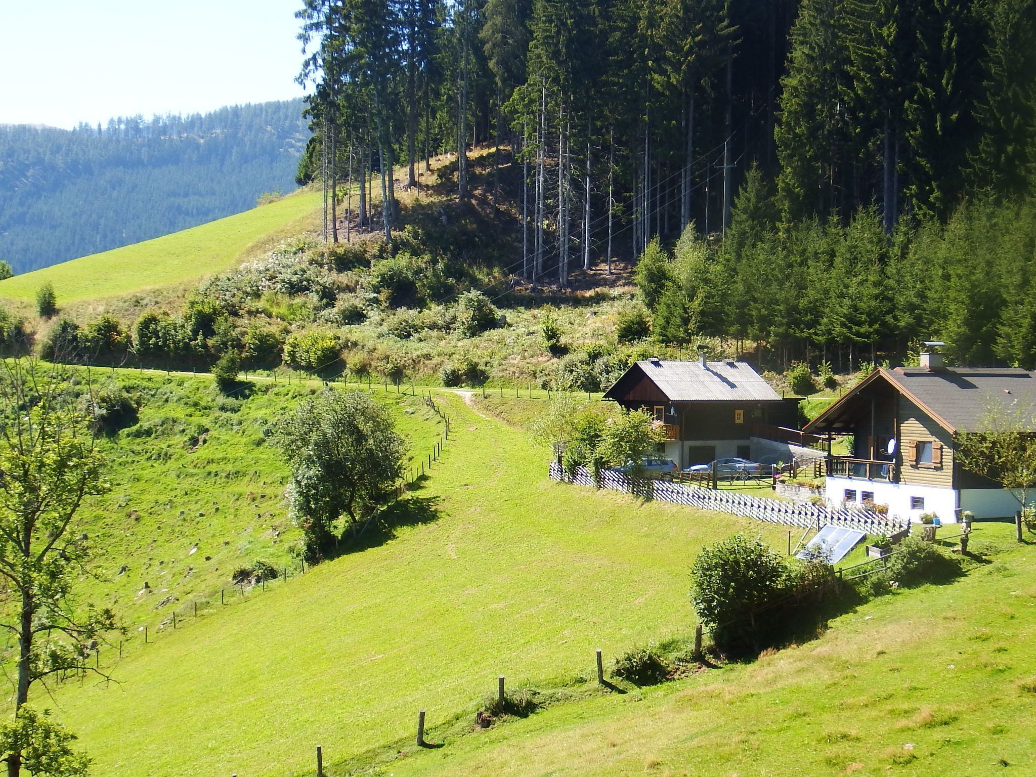Ein Landhaus mit umzäuntem Garten, umgeben von üppiger Vegetation und einem bewaldeten Hang.