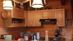 Interior de una cabaña de madera con una zona de cocina que incluye armarios de madera, una cafetera y un lámpara colgante.