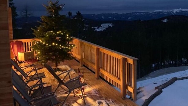 A wooden deck with chairs and a Christmas tree, overlooking a snowy landscape.