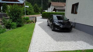 Een zwarte auto geparkeerd in een oprit, met een grindpad dat naar een huis leidt.