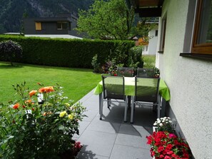 An outdoor patio with a table and chairs, surrounded by well-maintained flower beds and a hedge. - Rosa in Umhausen by Interhome (Umhausen)