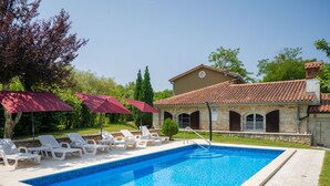 Ein rechteckiger Pool mit Fliesenrand, umgeben von Liegestühlen und roten Sonnenschirmen.