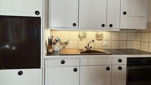 Una cocina con armarios blancos, un refrigerador negro, un fregadero y una estufa.