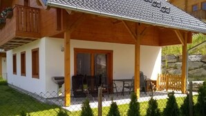 Une maison en bois dotée d’un patio couvert, d’une table à manger et de chaises.