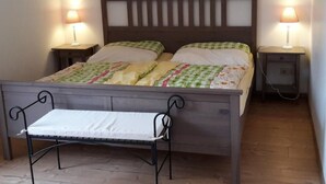 Un lit simple avec une tête de lit en bois, deux tables de chevet avec des lampes et un banc au pied du lit.