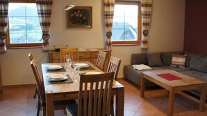 Un coin repas avec une table en bois dressée pour quatre personnes, encadrée par deux fenêtres ornées de rideaux.