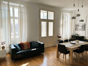 A modern living room with a black leather sofa, a wooden dining table with chairs, and large windows with white curtains. - Ausgefallene Wohnung by Interhome (Vienna)
