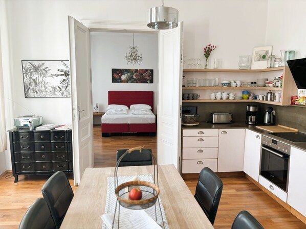 A modern kitchen with white cabinets, a dining table with chairs, and a red bed in the background. - Ausgefallene Wohnung by Interhome (Vienna)