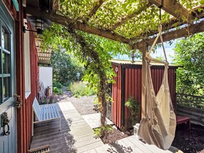 A wooden deck with a hanging hammock, a small garden area with plants, and a red building structure. - Niedliches Schwedenhaus. by Interhome (Mönsterås)