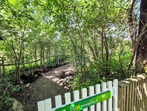 A pathway leading through a wooded area with a wooden fence and a sign indicating a location. - Niedliches Schwedenhaus. by Interhome (Mönsterås)