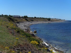 A coastal landscape with a rocky shoreline, a building with a sloped roof, and a clear blue sky. - Gemütliches Ferienhaus Sjöstugan am Meer by Interhome (Löttorp)