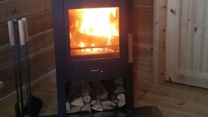Una estufa de leña con fuego a la vista, frente a una pared de madera.