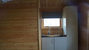 Una cocina compacta con paredes de madera, una ventana sobre el fregadero y un refrigerador.