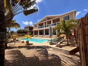 Una casa de dos pisos con piscina, palmeras y un porche techado.
