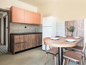 A modern kitchen with wooden cabinets, a white refrigerator, and a dining table set for four. - Modernes Studio für 3 Personen, Pool- und Gartenblick by Interhome (Gerakini)