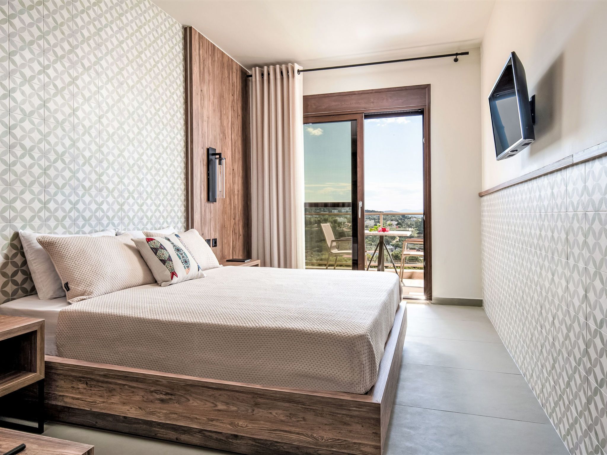Une chambre à coucher avec un lit, une table de chevet en bois, un téléviseur fixé au mur et un balcon avec vue.