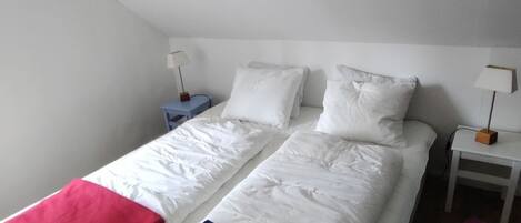 A bedroom with two beds, white bedding, and bedside tables with lamps.