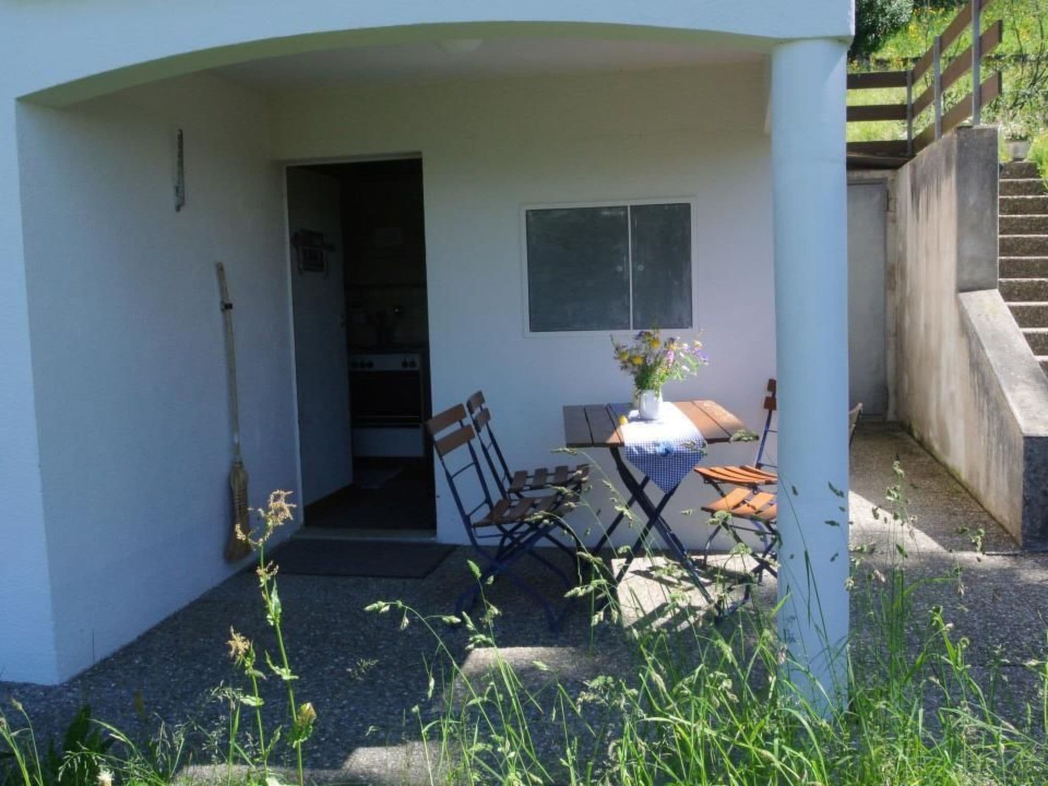 A small patio area with a table and chairs, a window, and a door leading to a kitchen.