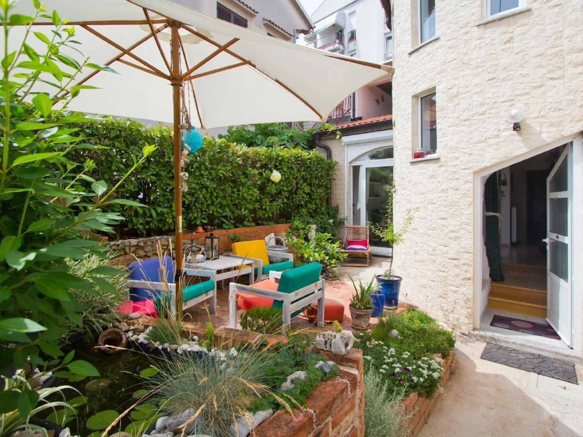 An outdoor patio area with a table and chairs, surrounded by greenery and a stone wall.