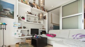 A living room with a white sofa, a black coffee table, a television, and a bookshelf filled with books and decorative items. - Wohnung in Rijeka mit Terrasse und Grill by Interhome (Rijeka)