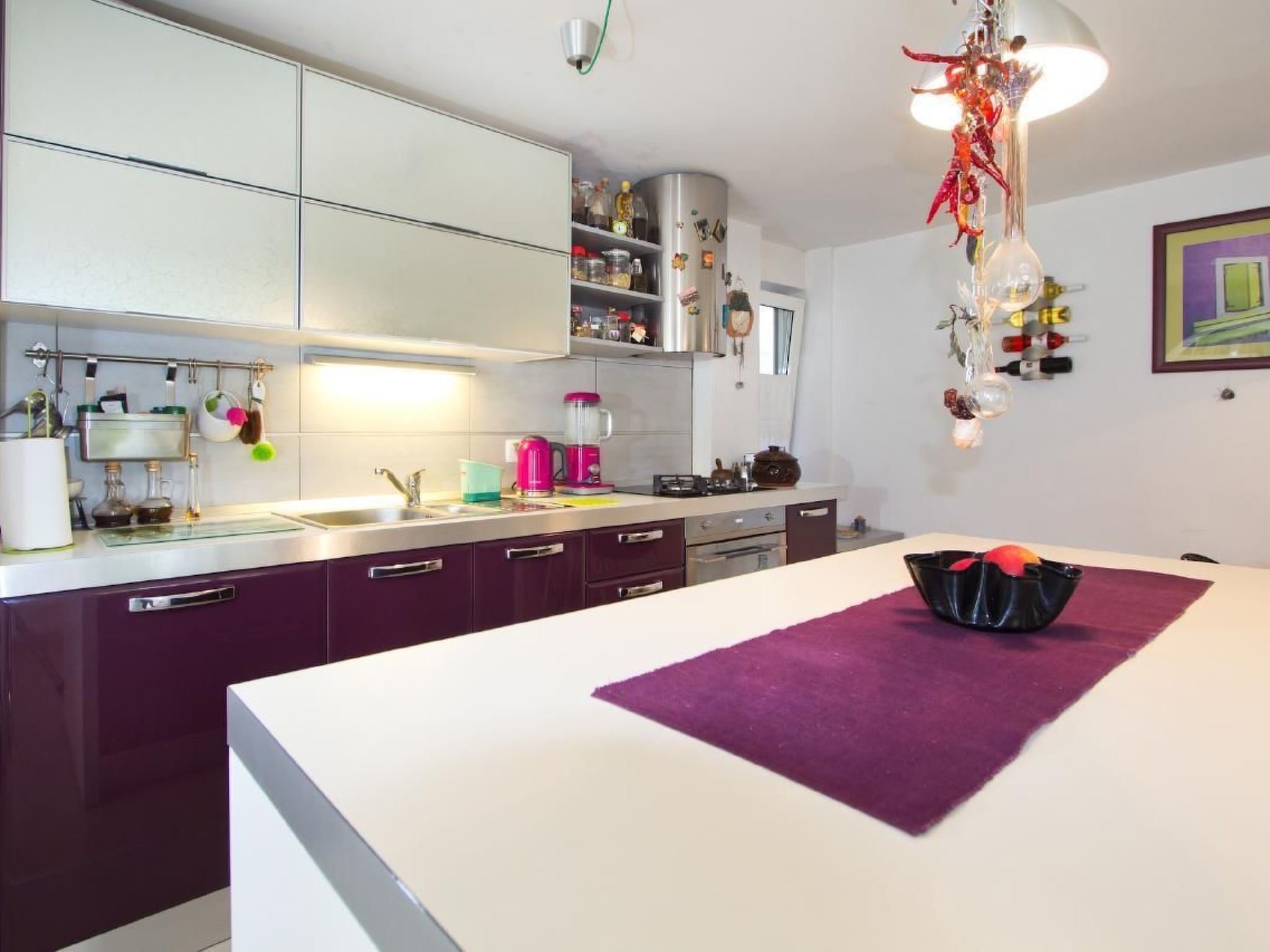 Una cocina moderna con encimeras blancas, un tapete púrpura y una lámpara colgante.