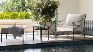 A poolside seating area with a chair and a small table, a covered bench, and a potted plant with flowers. - Chateau Duplex Ferme by Interhome (Marnand)