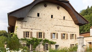 A large, rustic stone building with a sloped roof and multiple windows, surrounded by a well-maintained garden with flowering plants. - Chateau Duplex Ferme by Interhome (Marnand)