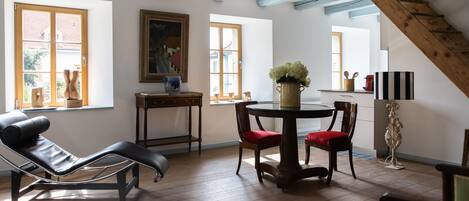 A room with a black leather chair, a wooden table with a vase, and a painting on the wall.