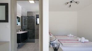 Ein modernes Badezimmer mit Dusche, Waschbecken und Spiegel. Ein Bett mit Kissen und ein Nachttisch mit Lampe.