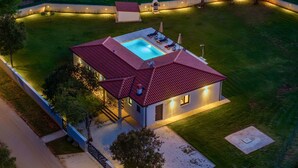 Ein modernes Haus mit Schwimmbad, umgeben von einem gut beleuchteten Garten und einem eingezäunten Bereich.