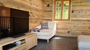 L’intérieur d’un chalet accueillant, avec un mur en bois, un canapé blanc, un téléviseur et une petite table.