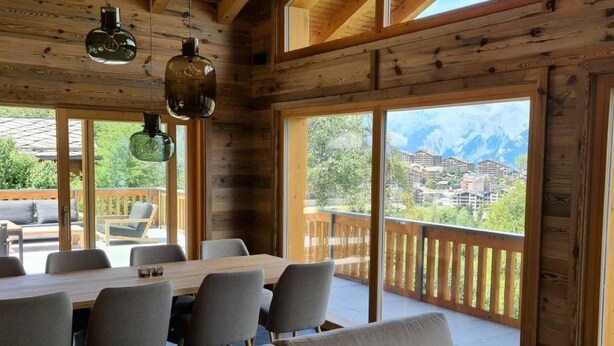 Une cabane en bois avec un coin repas, de grandes fenêtres et une vue sur les montagnes.